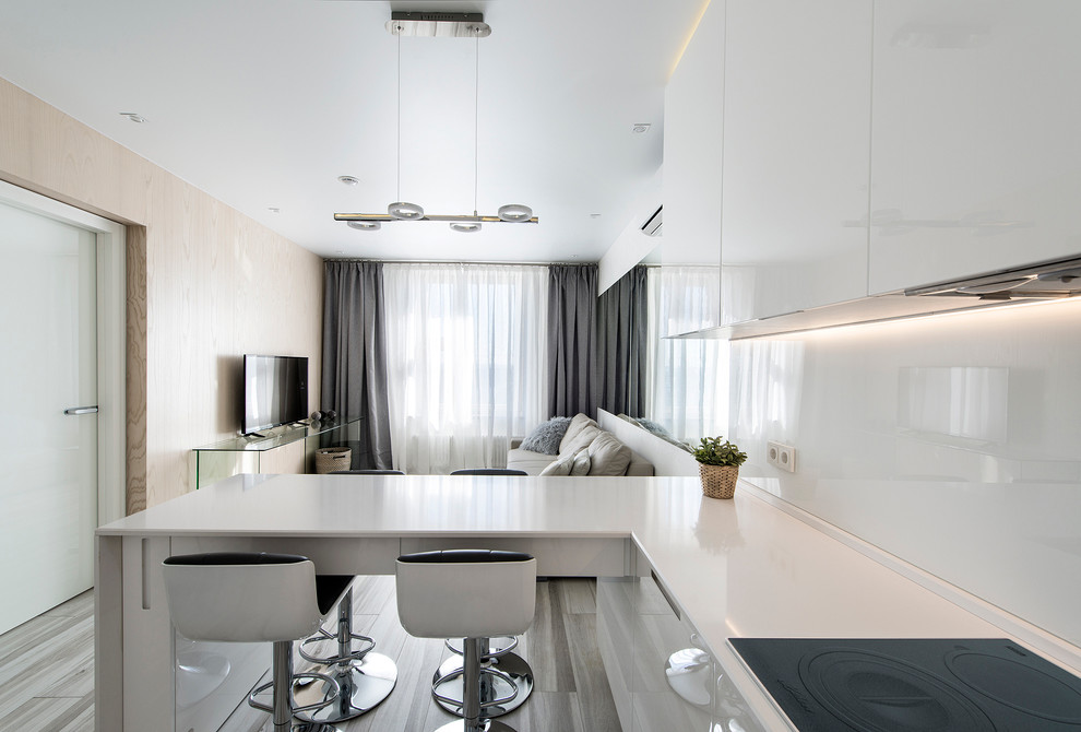 Example of a mid-sized trendy l-shaped medium tone wood floor open concept kitchen design in Palma de Mallorca with flat-panel cabinets, white cabinets, white backsplash and a peninsula