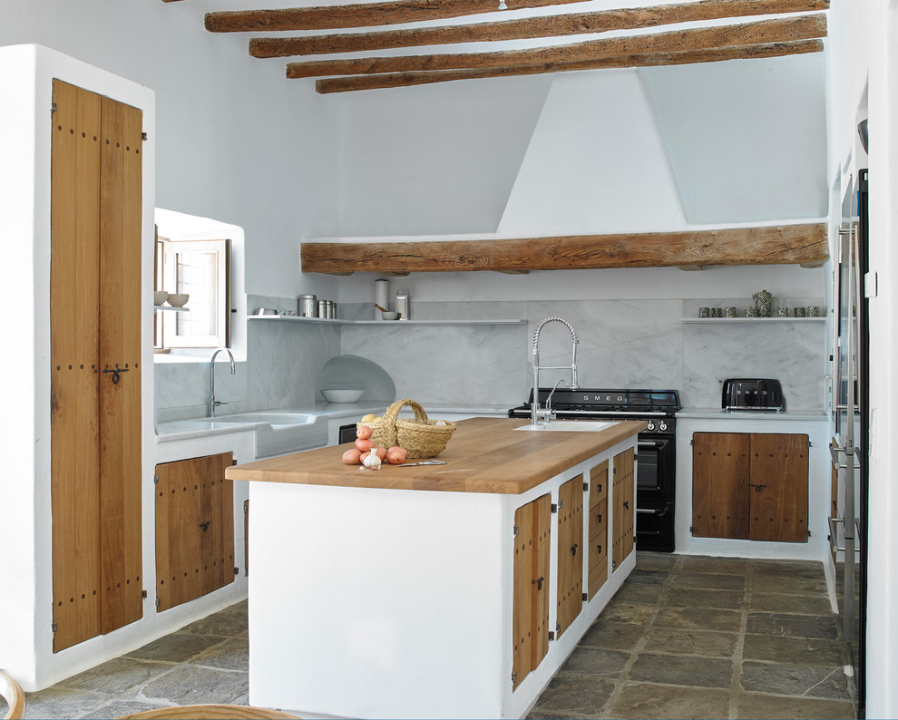 Inredning av ett medelhavsstil vit vitt u-kök, med en rustik diskho, släta luckor, skåp i mellenmörkt trä, vitt stänkskydd, stänkskydd i sten, svarta vitvaror, en köksö och brunt golv