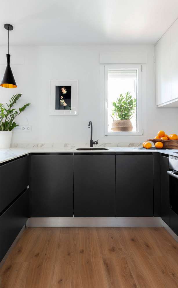 Стильный дизайн: п-образная кухня в скандинавском стиле с врезной мойкой, плоскими фасадами, черными фасадами, светлым паркетным полом, бежевым полом и белой столешницей - последний тренд