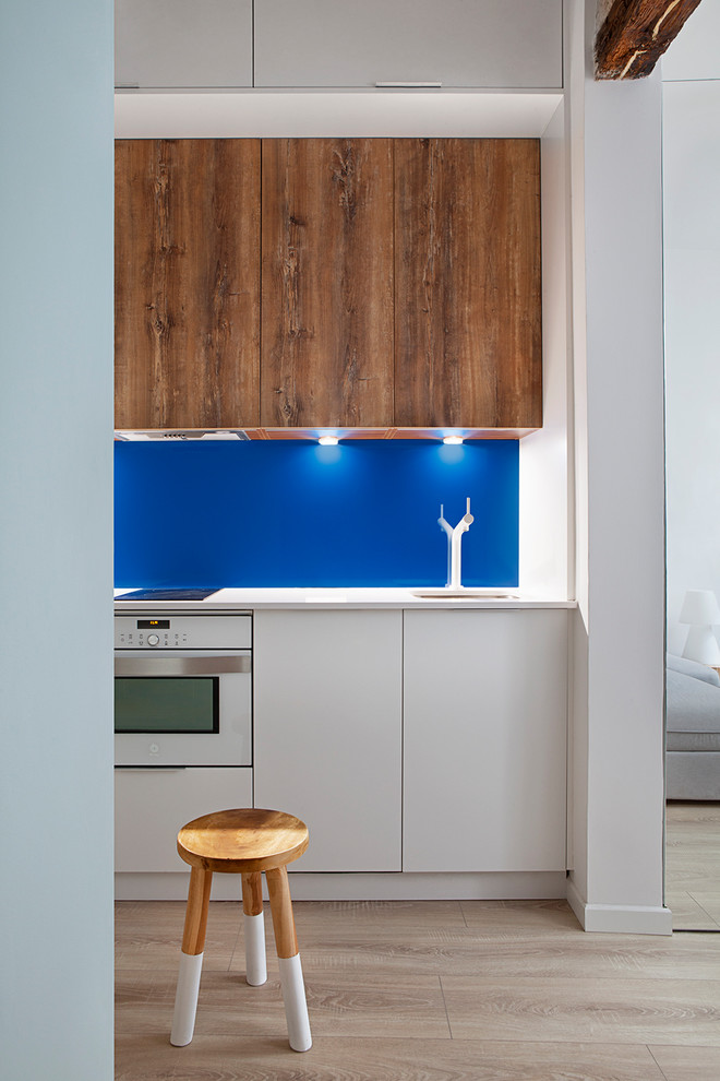 Kleine Skandinavische Küche mit Unterbauwaschbecken, hellbraunen Holzschränken, Küchenrückwand in Blau, weißen Elektrogeräten, hellem Holzboden und weißer Arbeitsplatte in Madrid