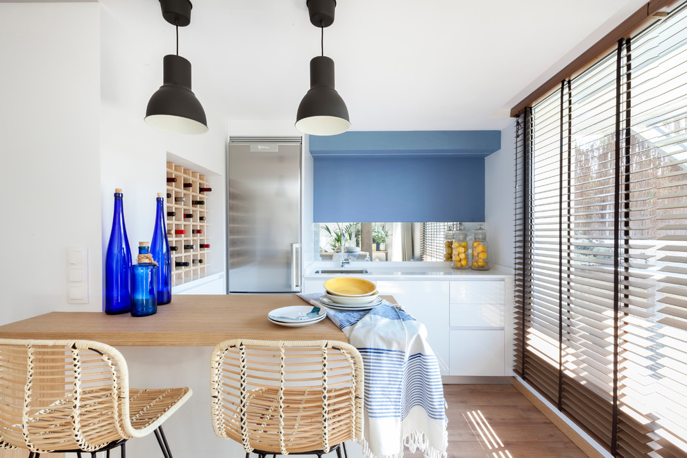 Modern inredning av ett linjärt kök, med en undermonterad diskho, släta luckor, vita skåp, träbänkskiva, blått stänkskydd, spegel som stänkskydd, rostfria vitvaror, mellanmörkt trägolv, en halv köksö och brunt golv