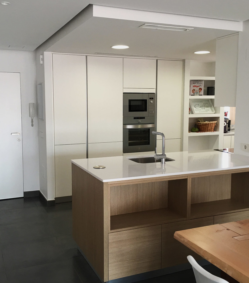Foto på ett litet funkis linjärt kök och matrum, med en enkel diskho, släta luckor, vita skåp, rostfria vitvaror och en köksö