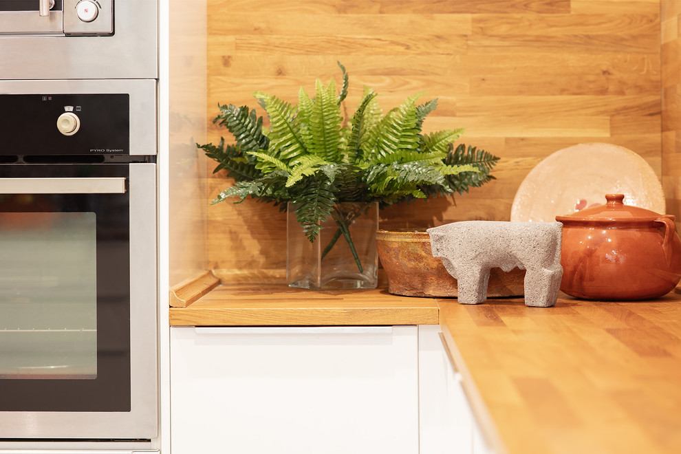 This is an example of a medium sized eclectic l-shaped kitchen/diner in Bilbao with an integrated sink, flat-panel cabinets, white cabinets, wood worktops, brown splashback, wood splashback, integrated appliances, concrete flooring, a breakfast bar, grey floors and brown worktops.