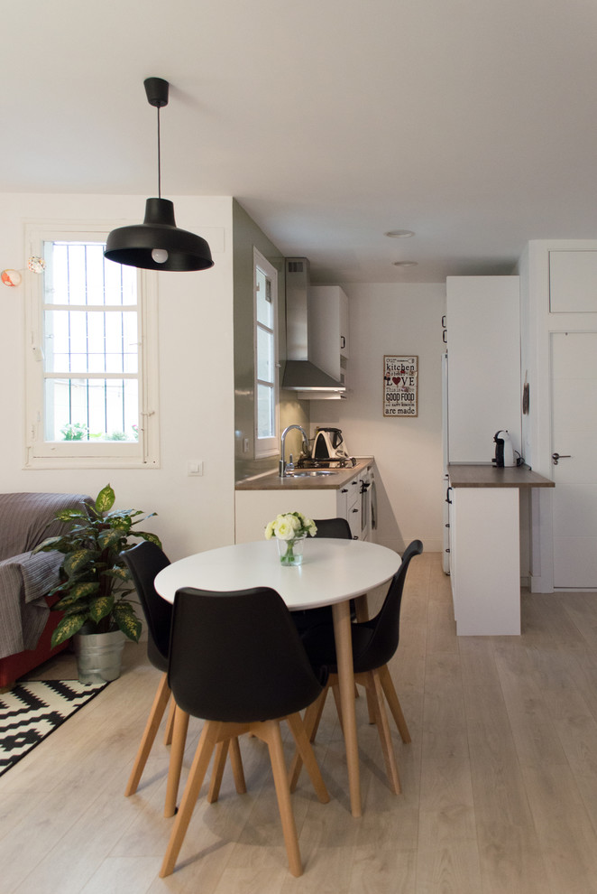 Foto på ett litet minimalistiskt linjärt kök med öppen planlösning, med ljust trägolv, en enkel diskho, luckor med profilerade fronter, vita skåp, träbänkskiva, grått stänkskydd, stänkskydd i cementkakel, vita vitvaror och beiget golv