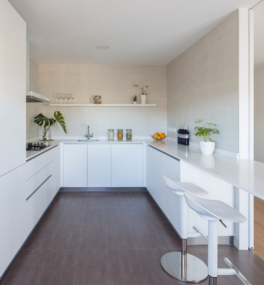 Modern inredning av ett vit vitt kök, med en undermonterad diskho, släta luckor, vita skåp, beige stänkskydd, integrerade vitvaror, en halv köksö och brunt golv