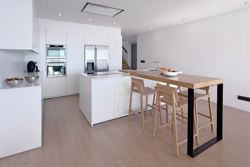 Bild på ett stort minimalistiskt linjärt kök med öppen planlösning, med släta luckor, vita skåp, vitt stänkskydd, rostfria vitvaror, mellanmörkt trägolv, en köksö, beiget golv och en undermonterad diskho