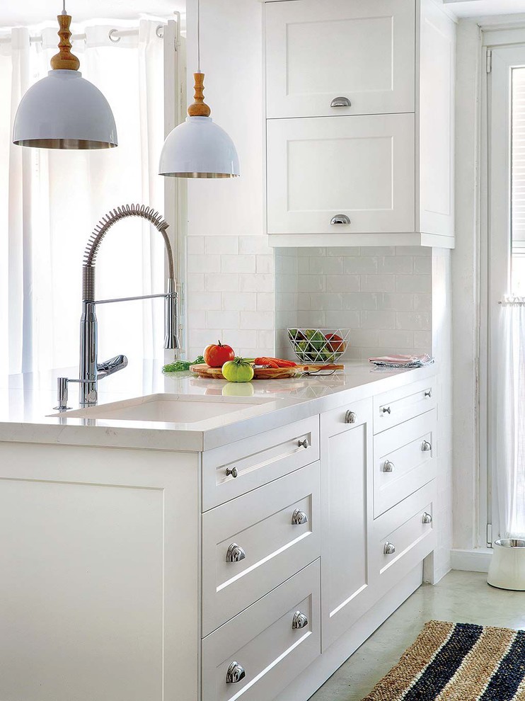 This is an example of a medium sized shabby-chic style u-shaped open plan kitchen in Madrid with a submerged sink, shaker cabinets, white cabinets, engineered stone countertops, white splashback, metro tiled splashback, white appliances, concrete flooring, a breakfast bar, grey floors and white worktops.