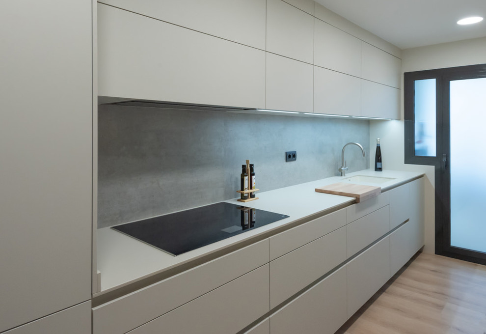 This is an example of a medium sized contemporary galley enclosed kitchen in Barcelona with an integrated sink, flat-panel cabinets, beige cabinets, grey splashback, integrated appliances, light hardwood flooring, no island, brown floors and beige worktops.