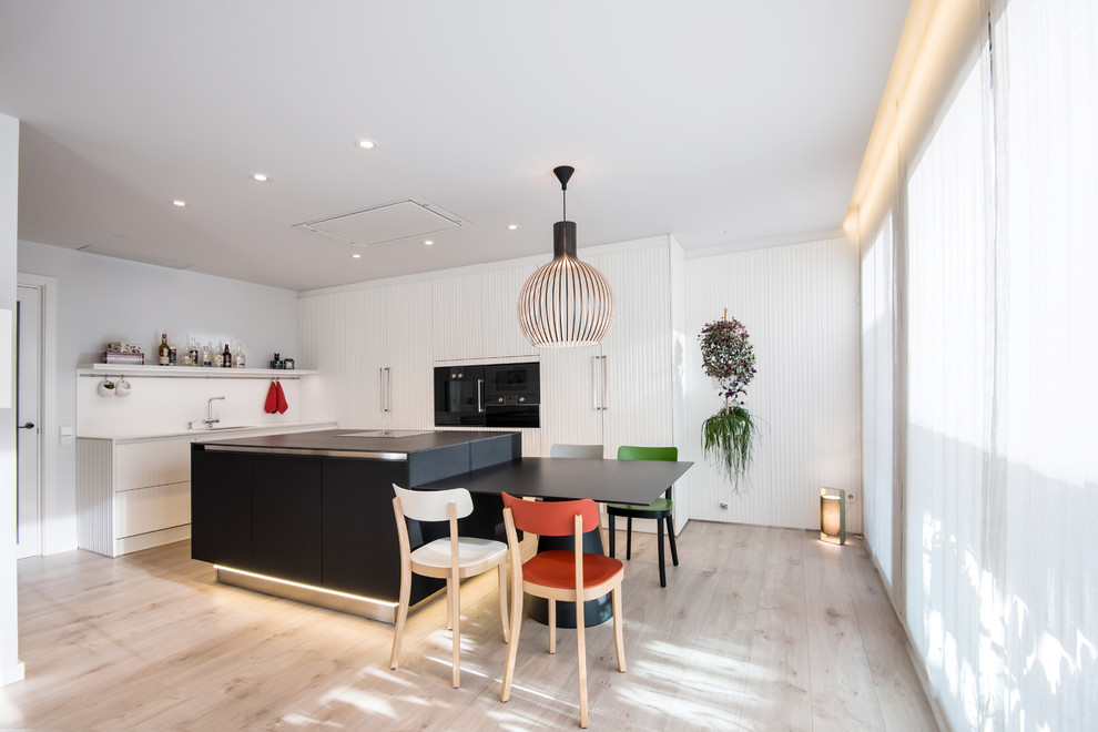 Moderne Wohnküche mit weißen Schränken, Küchenrückwand in Weiß, schwarzen Elektrogeräten, Kücheninsel, braunem Boden und Waschbecken in Barcelona