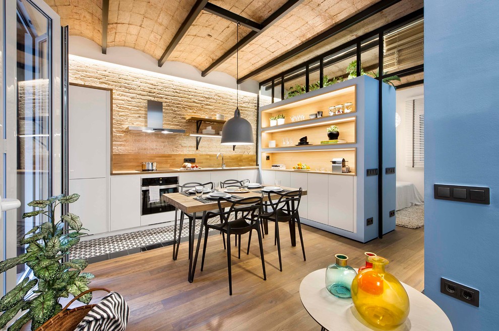 Diseño de cocina mediterránea con armarios abiertos, salpicadero beige, electrodomésticos negros, suelo de madera clara, suelo beige y con blanco y negro