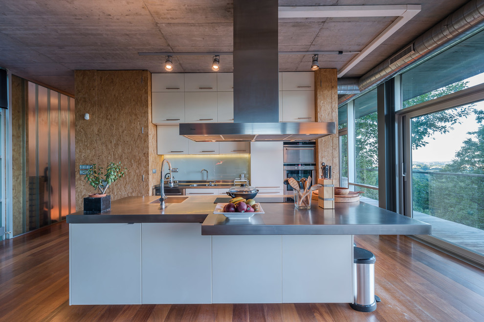 Imagen de cocina industrial grande abierta con fregadero de un seno, armarios con paneles lisos, electrodomésticos de acero inoxidable, suelo de madera en tonos medios y una isla