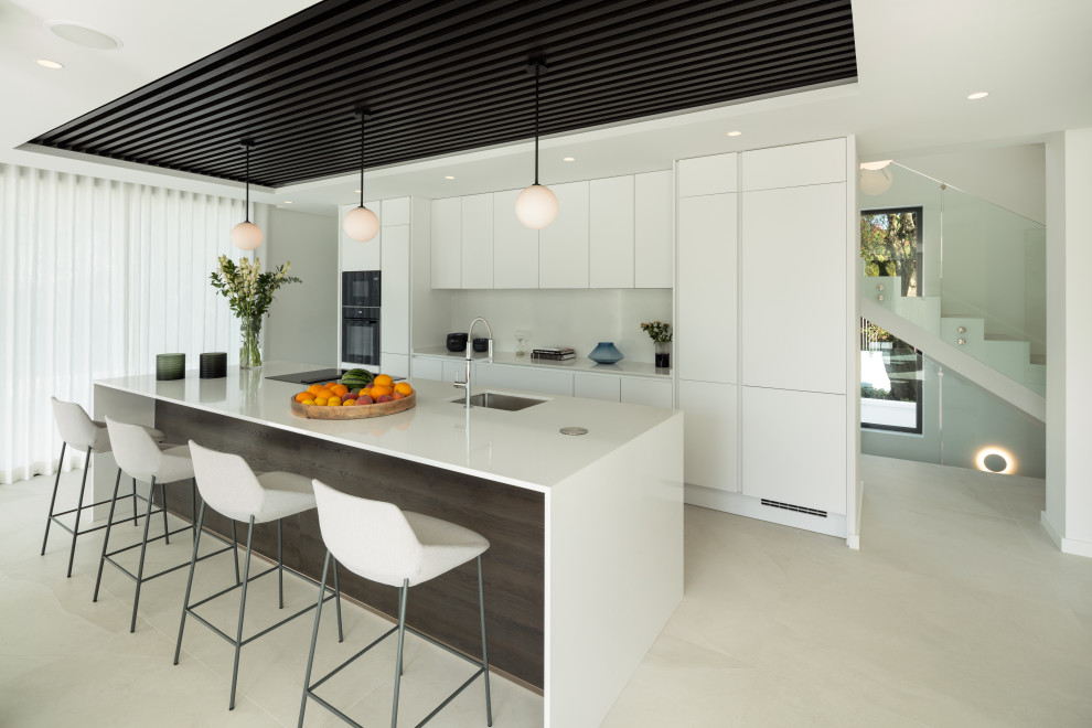 This is an example of a large mediterranean galley kitchen in Other with a submerged sink, flat-panel cabinets, white cabinets, white splashback, integrated appliances, an island, grey floors and white worktops.