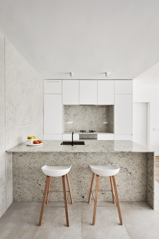 Moderne Küche mit Unterbauwaschbecken, flächenbündigen Schrankfronten, weißen Schränken, Küchenrückwand in Grau, Küchengeräten aus Edelstahl, Halbinsel und grauem Boden in Barcelona