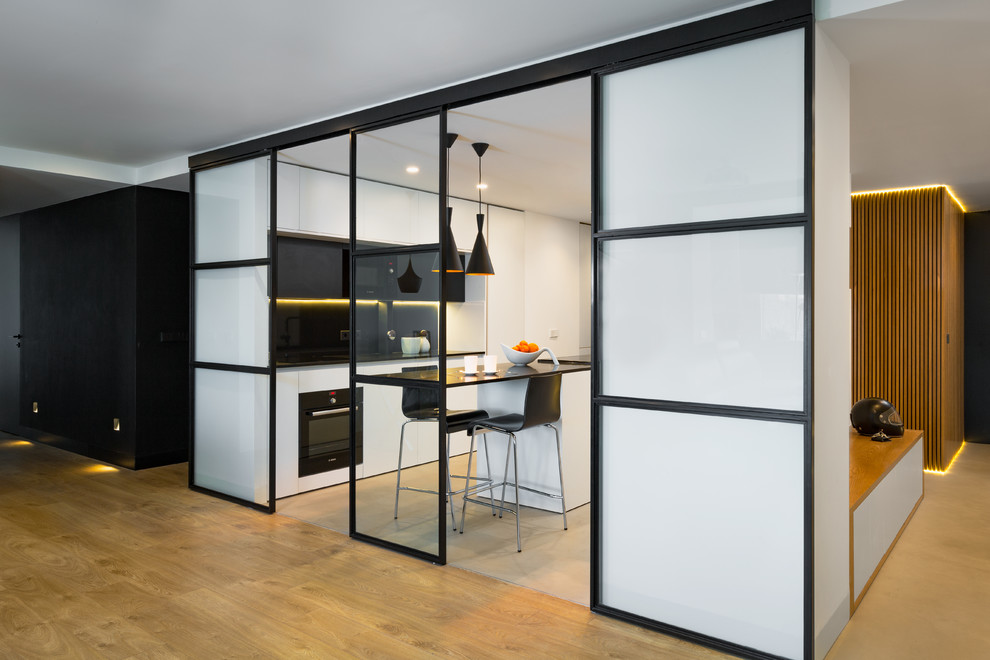 This is an example of a medium sized contemporary galley open plan kitchen in Madrid with a submerged sink, flat-panel cabinets, white cabinets, engineered stone countertops, black splashback, marble splashback, black appliances, concrete flooring, an island, grey floors and black worktops.