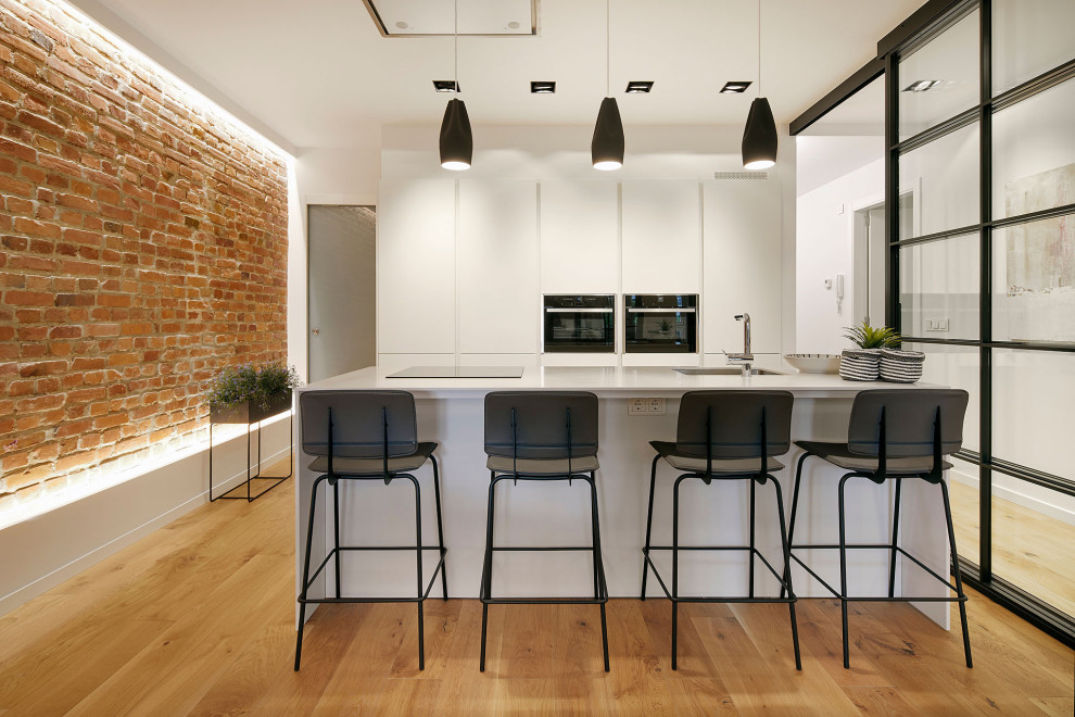 Immagine di una cucina design di medie dimensioni con lavello sottopiano, ante lisce, ante bianche, elettrodomestici da incasso, pavimento marrone e top bianco
