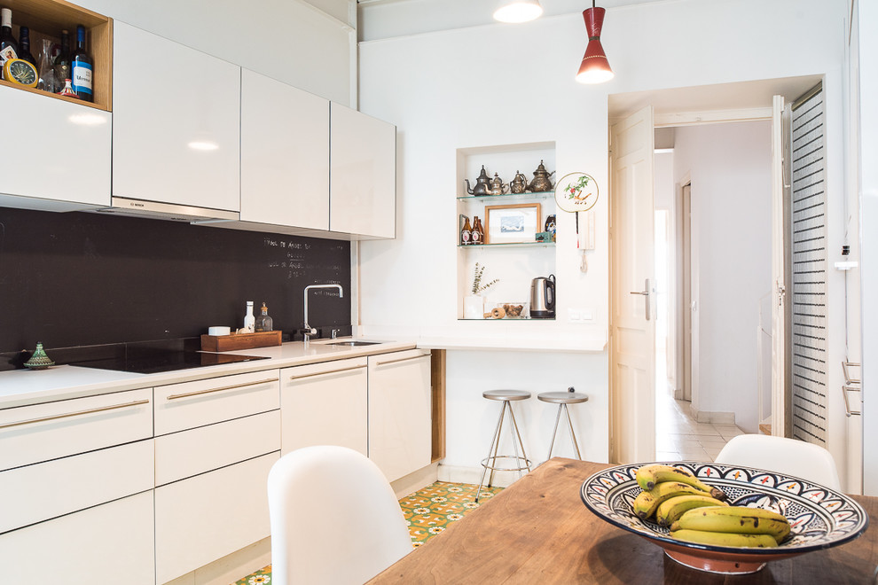 Bild på ett mellanstort eklektiskt linjärt kök och matrum, med släta luckor, vita skåp, svart stänkskydd, klinkergolv i keramik och flerfärgat golv
