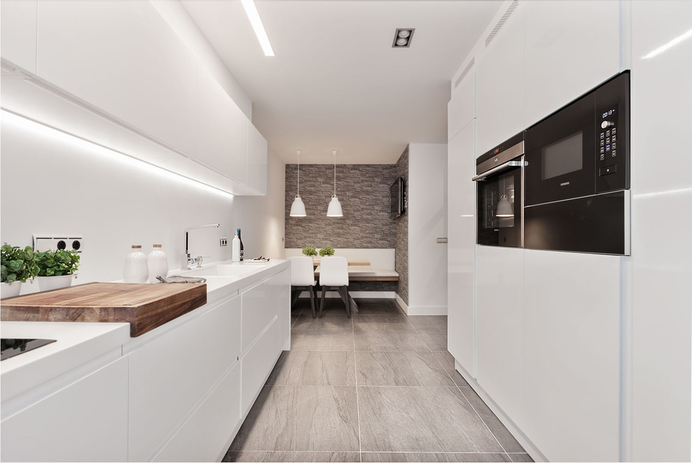 Einzeilige, Große Moderne Wohnküche ohne Insel mit flächenbündigen Schrankfronten, weißen Schränken, Küchenrückwand in Weiß, schwarzen Elektrogeräten, grauem Boden und weißer Arbeitsplatte in Bilbao