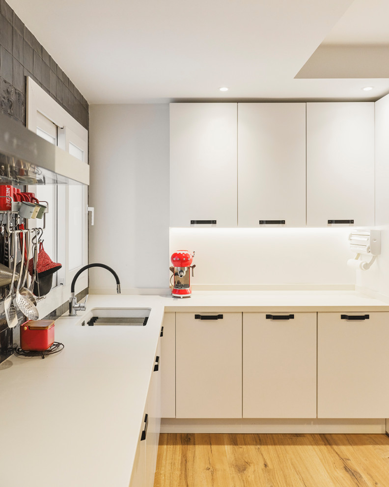 Photo of a medium sized scandi single-wall kitchen/diner in Other with a single-bowl sink, shaker cabinets, white cabinets, engineered stone countertops, white splashback, ceramic splashback, integrated appliances, medium hardwood flooring, no island, brown floors and white worktops.