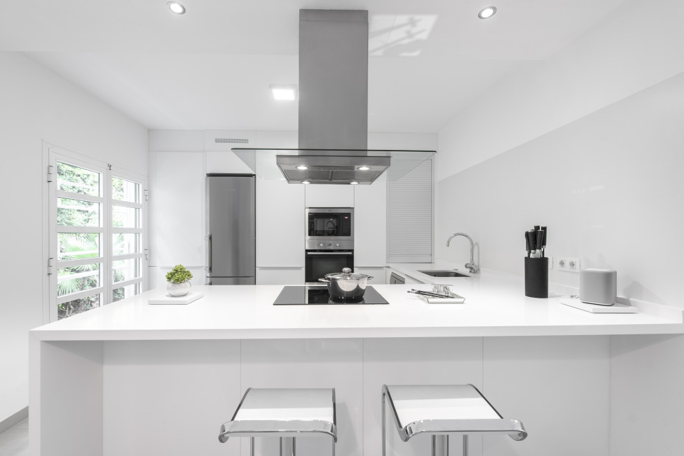 Modern inredning av ett vit vitt u-kök, med en undermonterad diskho, släta luckor, vita skåp, rostfria vitvaror, en halv köksö och grått golv