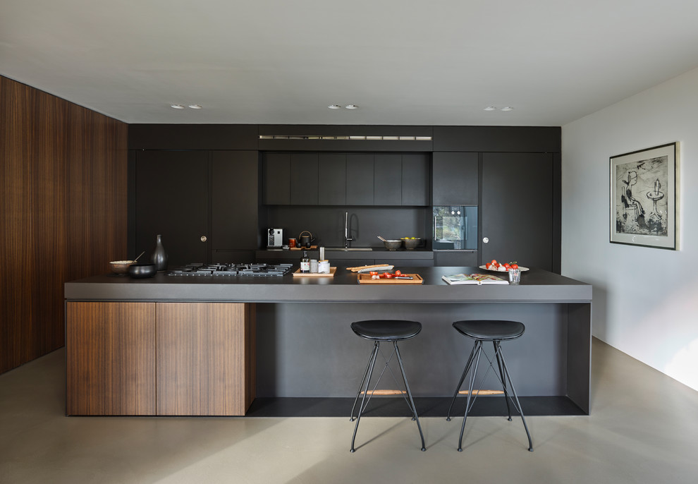 Foto di un cucina con isola centrale minimal con lavello sottopiano, ante lisce, ante nere, paraspruzzi nero, pavimento grigio e top nero