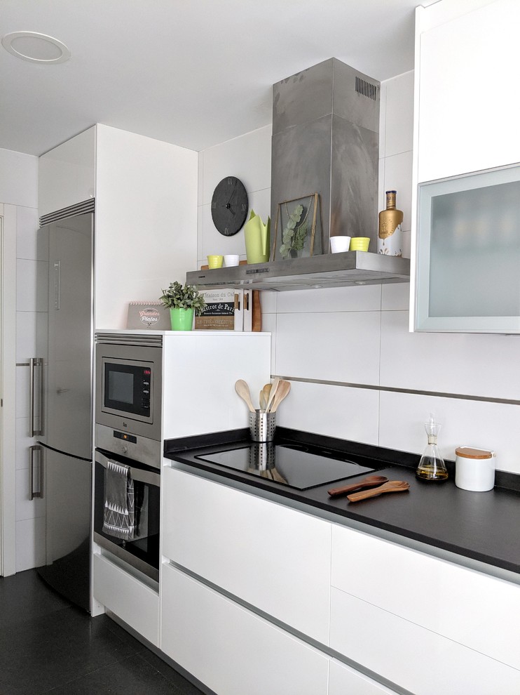 Bild på ett avskilt, mellanstort skandinaviskt svart svart u-kök, med en nedsänkt diskho, släta luckor, vita skåp, granitbänkskiva, vitt stänkskydd, stänkskydd i porslinskakel, rostfria vitvaror, klinkergolv i porslin och svart golv