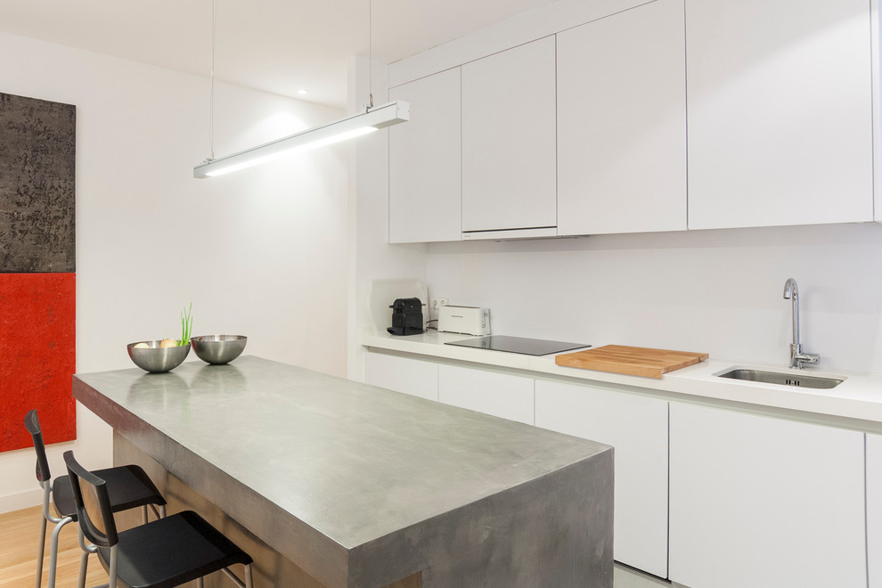 Photo of a medium sized contemporary galley enclosed kitchen in Madrid with a submerged sink, flat-panel cabinets, white cabinets, white splashback, an island, concrete worktops, stainless steel appliances and light hardwood flooring.