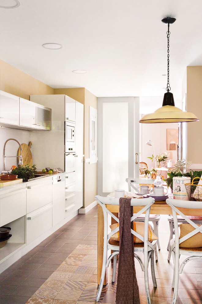 Bild på ett stort shabby chic-inspirerat linjärt kök och matrum, med skåp i shakerstil, vita skåp, rostfria vitvaror, klinkergolv i keramik och brunt golv