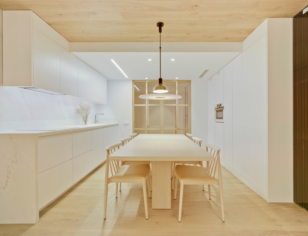 This is an example of a medium sized contemporary kitchen/diner in Other with flat-panel cabinets, white cabinets, white splashback, white appliances, light hardwood flooring, no island, beige floors, white worktops and stone slab splashback.