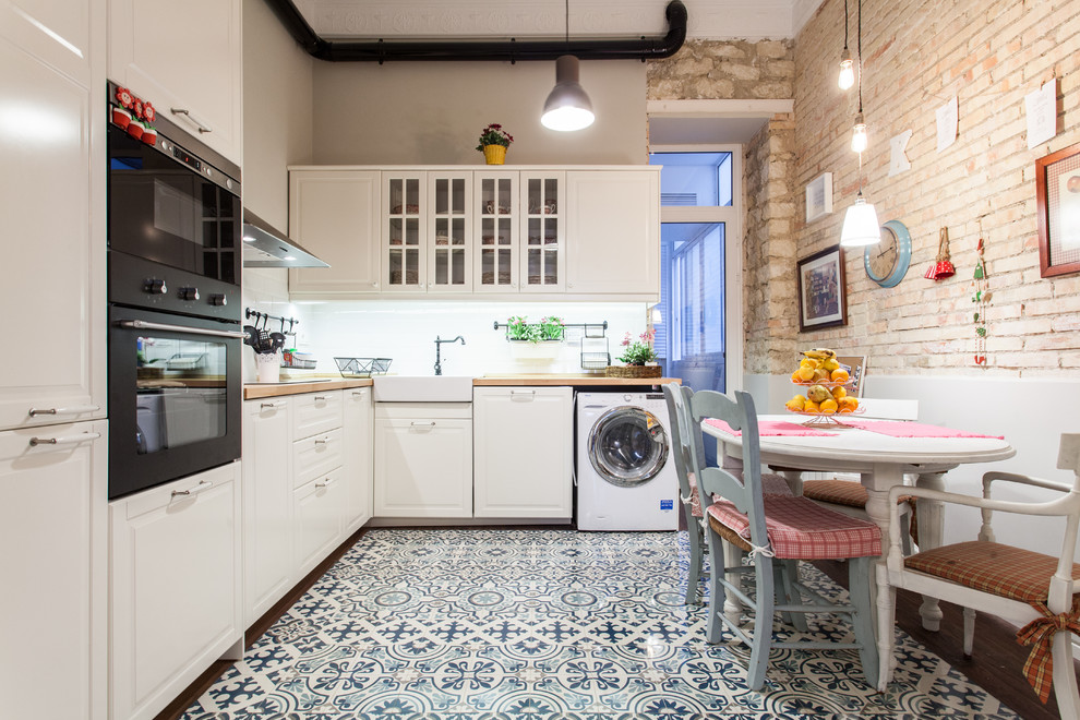 Exempel på ett mellanstort klassiskt kök, med en rustik diskho, vita skåp, träbänkskiva, vitt stänkskydd, svarta vitvaror, klinkergolv i keramik, luckor med glaspanel och flerfärgat golv