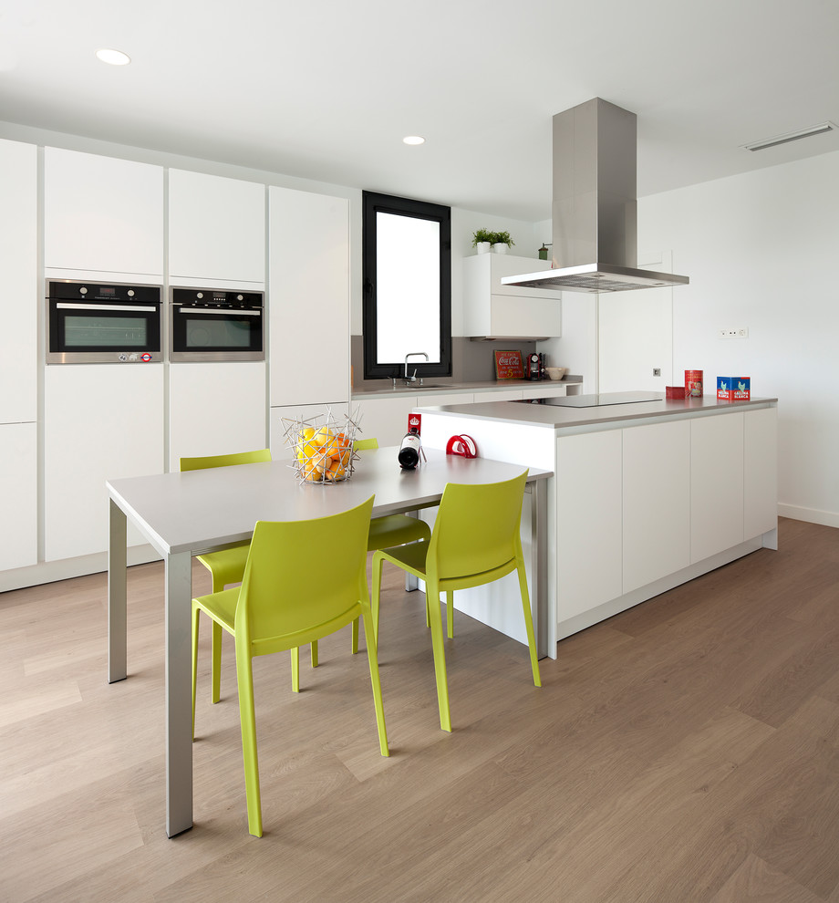 This is an example of a contemporary kitchen in Valencia with a single-bowl sink, flat-panel cabinets, white cabinets, grey splashback, stainless steel appliances, light hardwood flooring, an island, beige floors and grey worktops.