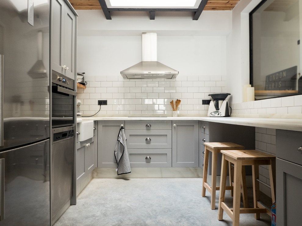 Exempel på ett avskilt, mellanstort klassiskt u-kök, med luckor med infälld panel, grå skåp, vitt stänkskydd, stänkskydd i tunnelbanekakel, rostfria vitvaror, betonggolv och en rustik diskho