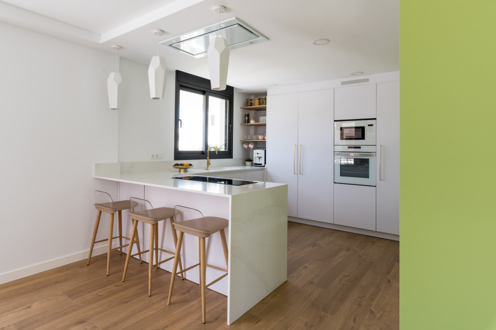 Example of a mid-sized trendy u-shaped laminate floor and brown floor eat-in kitchen design in Madrid with an undermount sink, flat-panel cabinets, white cabinets, quartz countertops, white backsplash, white appliances, a peninsula and white countertops