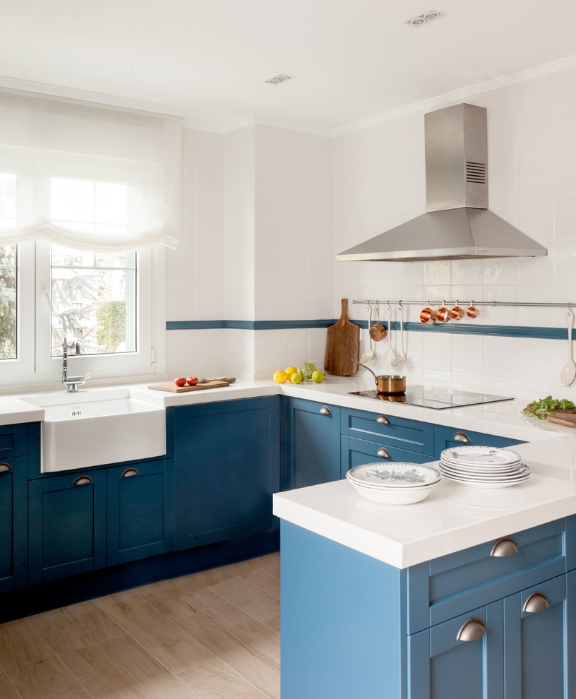 Mittelgroße Maritime Küche in U-Form mit blauen Schränken, Küchenrückwand in Weiß, Rückwand aus Keramikfliesen, Halbinsel, Landhausspüle, Schrankfronten im Shaker-Stil und beigem Boden in Bilbao