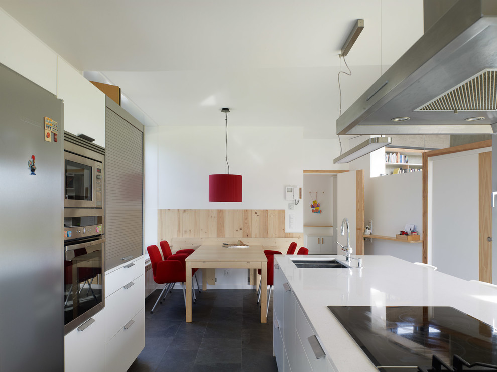 Cette image montre une cuisine design avec un évier encastré, un placard à porte plane, des portes de placard blanches, un plan de travail en quartz modifié, un électroménager en acier inoxydable, îlot et un sol gris.