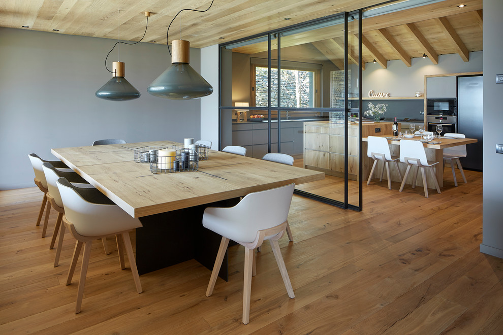 Cette photo montre une grande salle à manger ouverte sur le salon nature avec parquet clair, un mur gris et un sol marron.