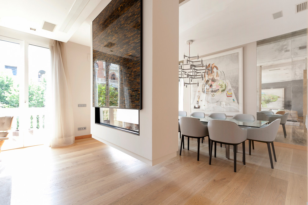 Foto di una sala da pranzo aperta verso il soggiorno design di medie dimensioni con pareti bianche, parquet chiaro e camino bifacciale