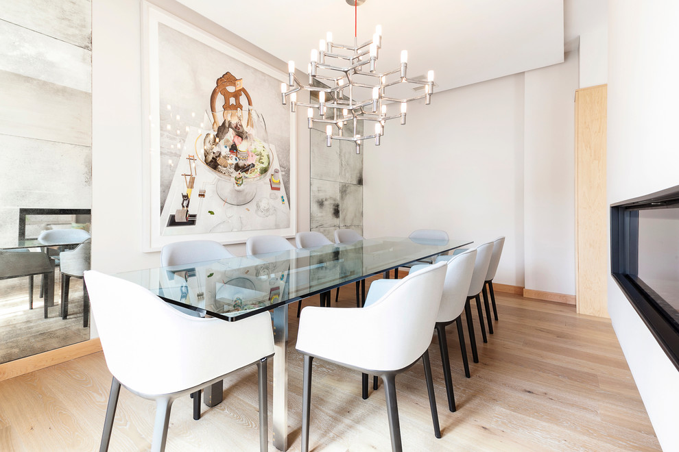 Medium sized contemporary open plan dining room in Madrid with white walls, light hardwood flooring and a ribbon fireplace.