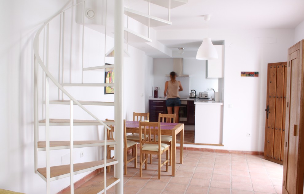 Aménagement d'une petite salle à manger ouverte sur la cuisine méditerranéenne avec un mur blanc et tomettes au sol.