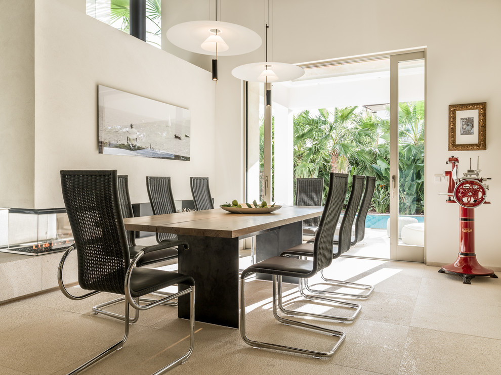 This is an example of a beach style dining room in Palma de Mallorca with white walls, a two-sided fireplace and beige floors.
