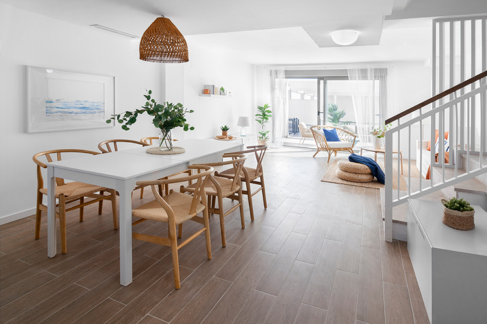 Aménagement d'une salle à manger ouverte sur le salon bord de mer avec un mur blanc et un sol marron.