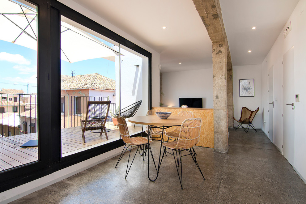 Foto di una sala da pranzo aperta verso il soggiorno industriale con pareti bianche, pavimento in cemento e pavimento grigio