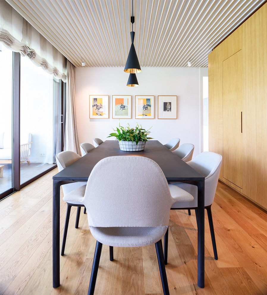 Immagine di una grande sala da pranzo minimalista chiusa con pareti bianche, pavimento in legno massello medio e nessun camino