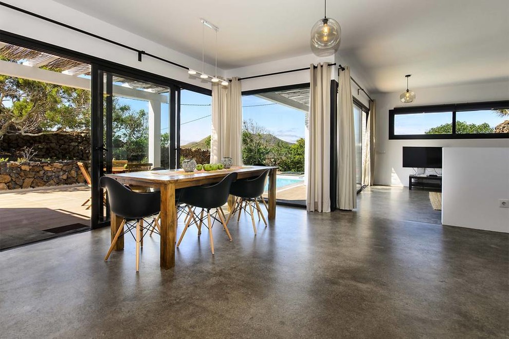 Foto di una sala da pranzo aperta verso il soggiorno minimalista con pareti bianche, pavimento in cemento, pavimento grigio e nessun camino