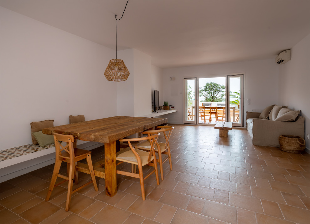 Idée de décoration pour une salle à manger ouverte sur le salon méditerranéenne de taille moyenne avec un mur blanc, tomettes au sol, une cheminée ribbon, un manteau de cheminée en brique et un sol marron.