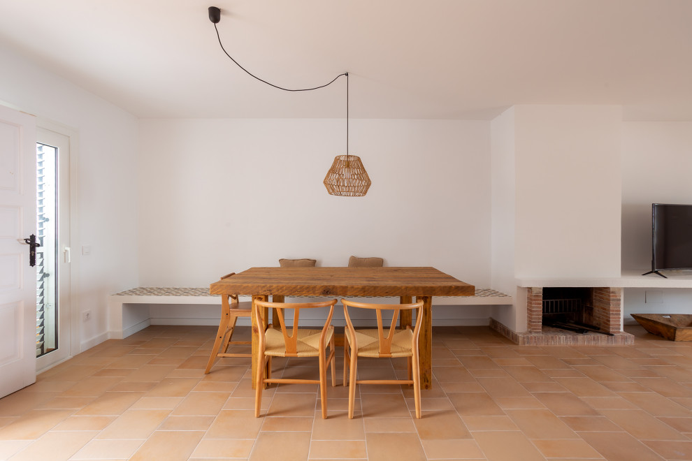 На фото: гостиная-столовая среднего размера в средиземноморском стиле с белыми стенами, полом из терракотовой плитки, горизонтальным камином, фасадом камина из кирпича и коричневым полом с