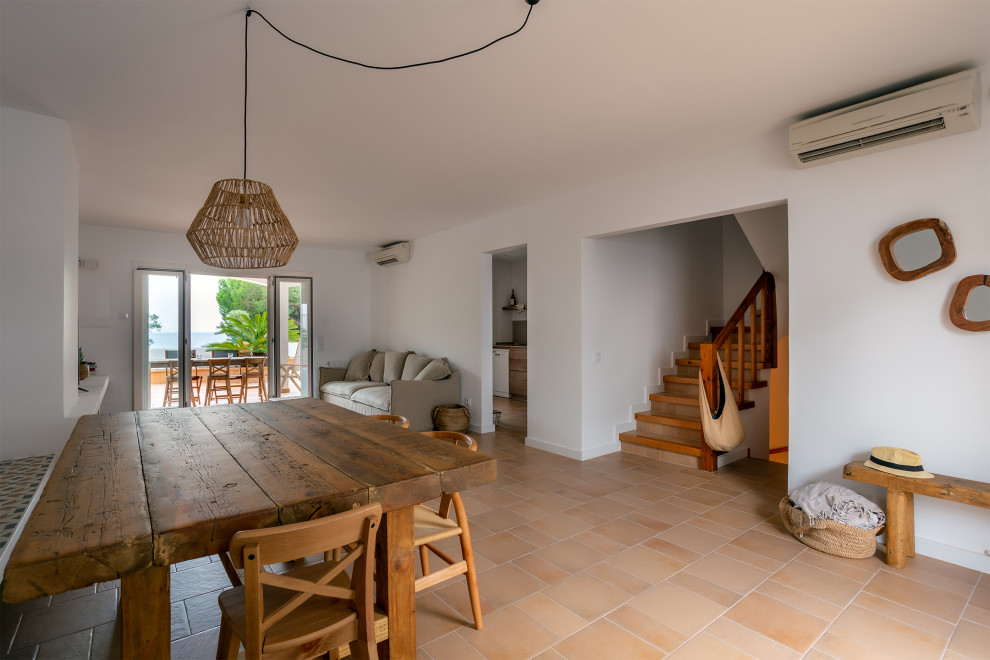 Exemple d'une salle à manger ouverte sur le salon méditerranéenne de taille moyenne avec un mur blanc, tomettes au sol, une cheminée ribbon, un manteau de cheminée en brique et un sol marron.