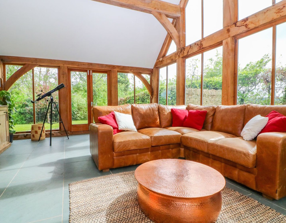Photo of a large country conservatory in Gloucestershire with slate flooring, a wood burning stove, a glass ceiling and grey floors.