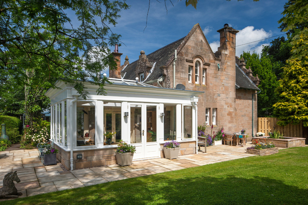 This is an example of a large traditional conservatory in Edinburgh with travertine flooring, a wood burning stove, a plastered fireplace surround, a skylight and beige floors.