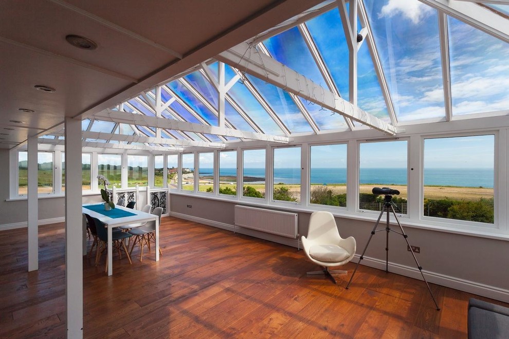 Large beach style conservatory in Kent with dark hardwood flooring and a glass ceiling.