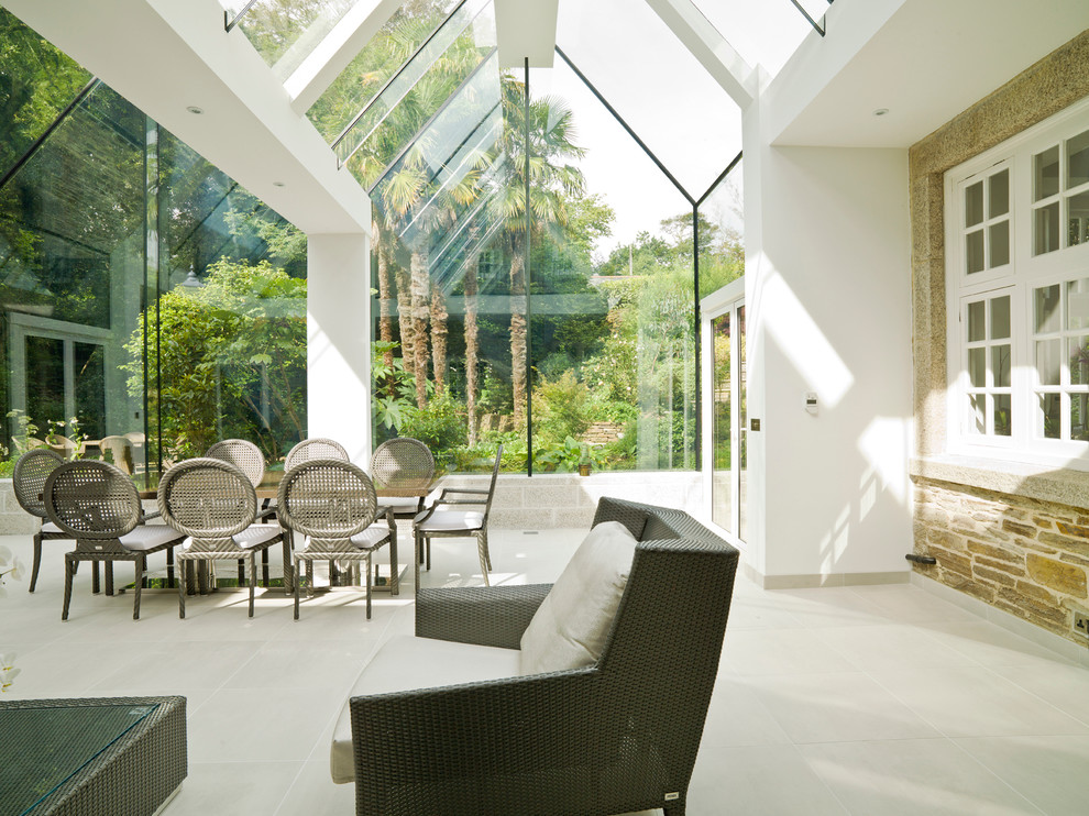 Inspiration pour une grande véranda design avec un sol en calcaire, un plafond en verre et un sol beige.